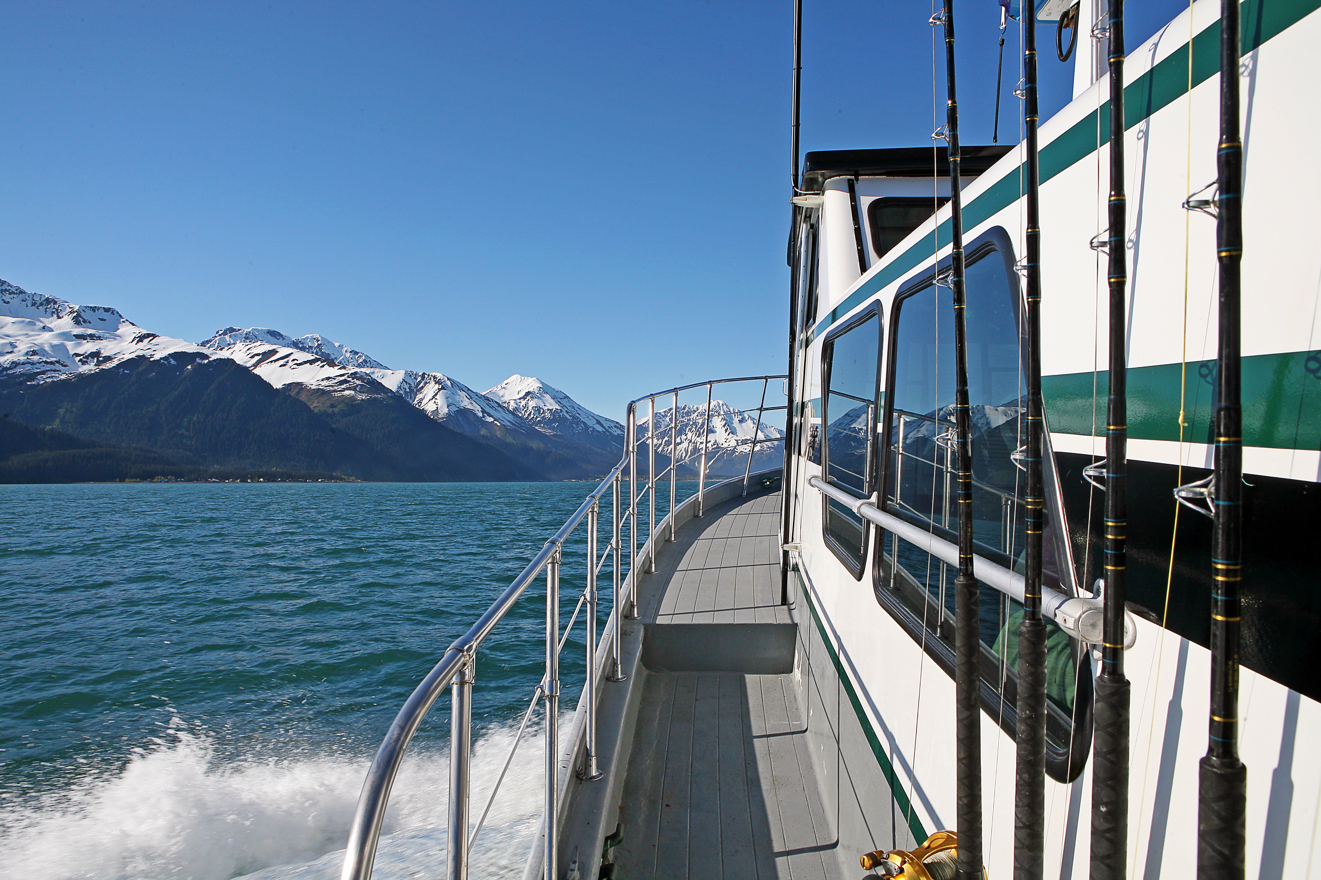 A view over water and a snowcapped mountain range from the side of a luxury boat in Alaska. 